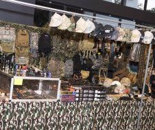 A camouflage table with a lot of hats and backpacks on it.