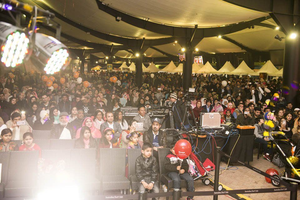 A large crowd of people are sitting in a large room watching a concert.