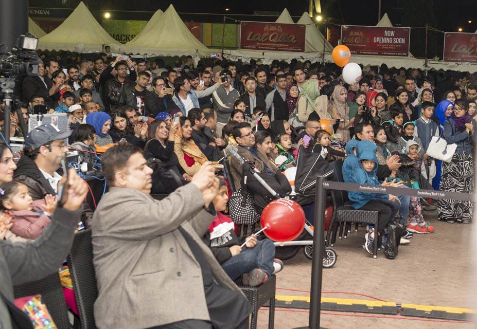 A crowd of people watching a show with a coca cola sign in the background