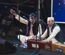 Two men are sitting on the floor playing instruments on a stage.