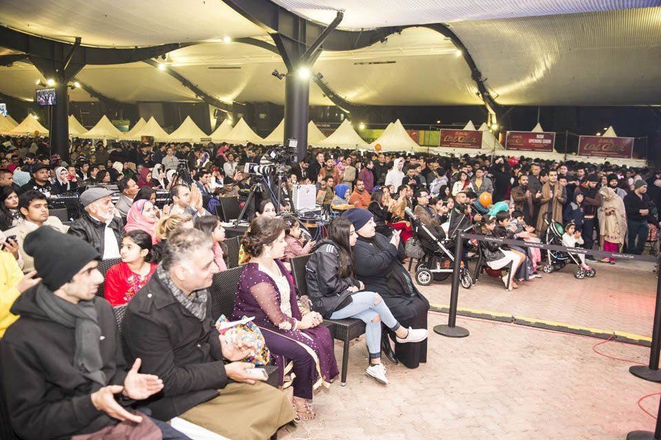 A large group of people are sitting in a tent watching a performance.