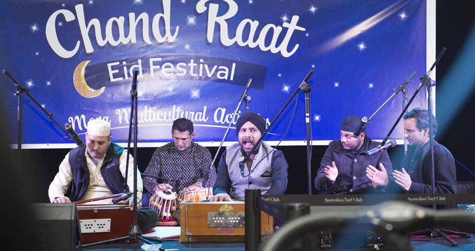 A group of men are sitting in front of a sign that says chand raat eid festival.