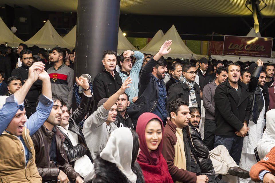 A crowd of people are sitting in front of a coca cola sign.