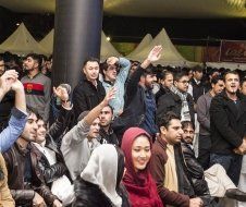 A crowd of people are sitting in a room with their hands in the air.