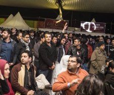 A large group of people are sitting under a tent at a concert.