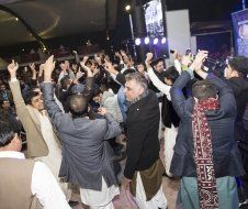 A group of people are dancing in a room with their arms in the air.