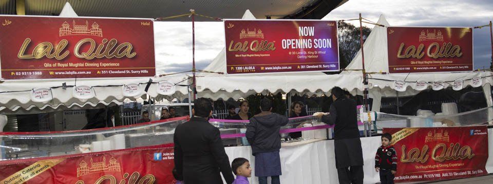 A group of people are standing in front of a food stand.