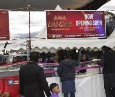 A group of people standing in front of a sign that says `` now opening soon ''.