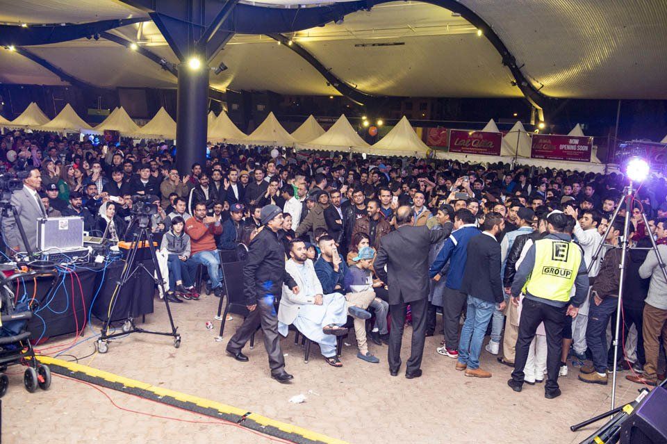 A crowd of people are gathered in a large room with a man in a yellow vest that says ' a ' on it