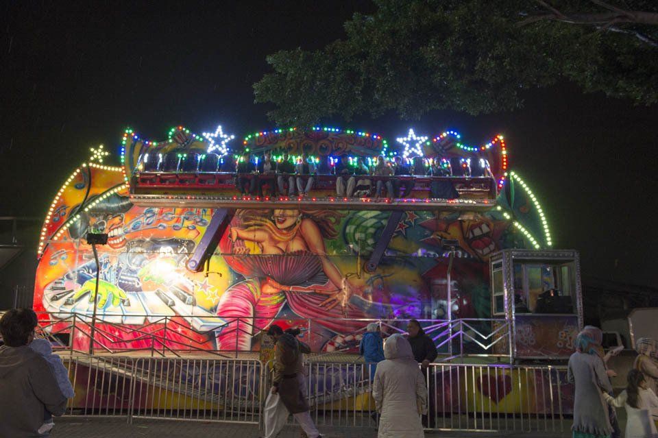 A group of people are standing in front of a carnival ride at night.
