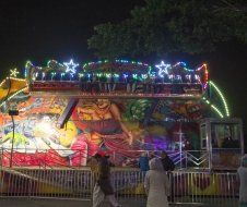 A group of people are standing in front of a carnival ride at night.