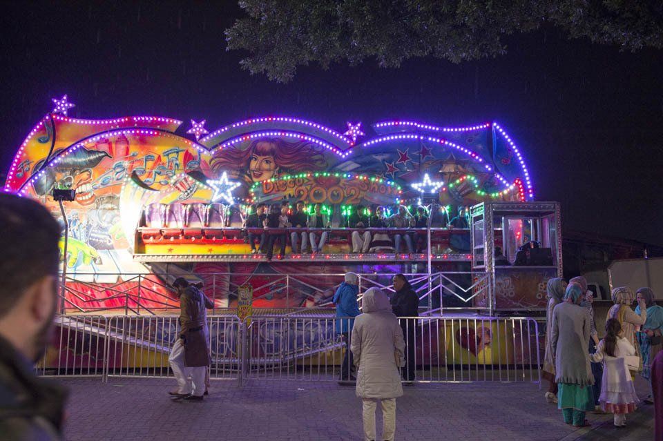 A group of people are standing in front of a carnival ride at night.