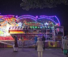 A group of people are standing in front of a carnival ride at night.