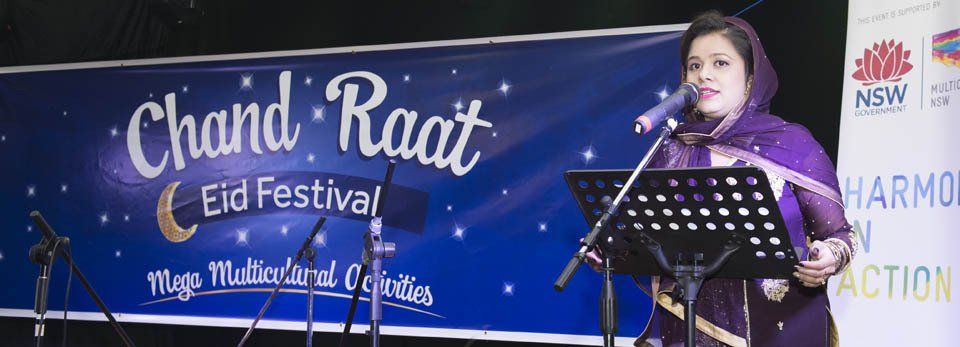 A woman is singing into a microphone in front of a banner that says chand raat eid festival.