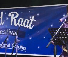 A person is singing into a microphone in front of a sign that says ' raat festival ' on it.