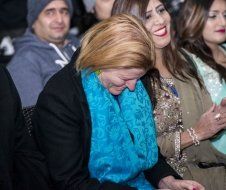 A woman in a blue scarf is sitting in a crowd of people.