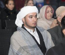 A man wearing a turban is sitting in a crowd of people.