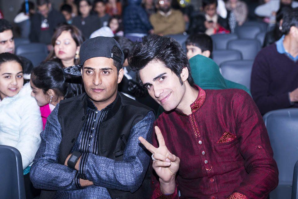 Two men are posing for a picture while sitting in a crowd of people.