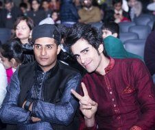 Two men are sitting next to each other in a theatre giving a peace sign.