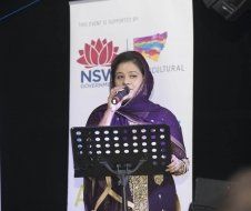 A woman is singing into a microphone in front of a sign that says nsw cultural.