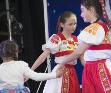 Three young girls in traditional costume are holding hands on a stage.