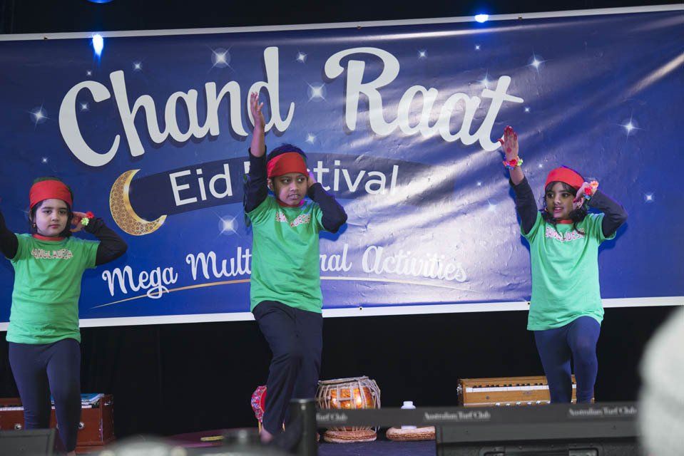 A group of children are dancing in front of a banner that says chand raat.