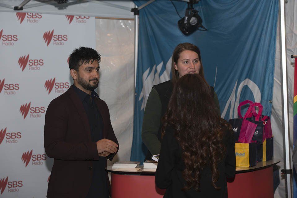 A man and a woman are standing in front of a table talking to each other.