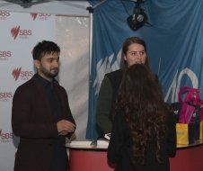 A man and a woman are standing in front of a table talking to each other.