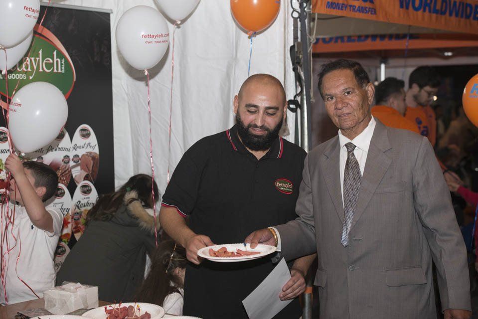 Two men are standing next to each other and one is holding a plate of food