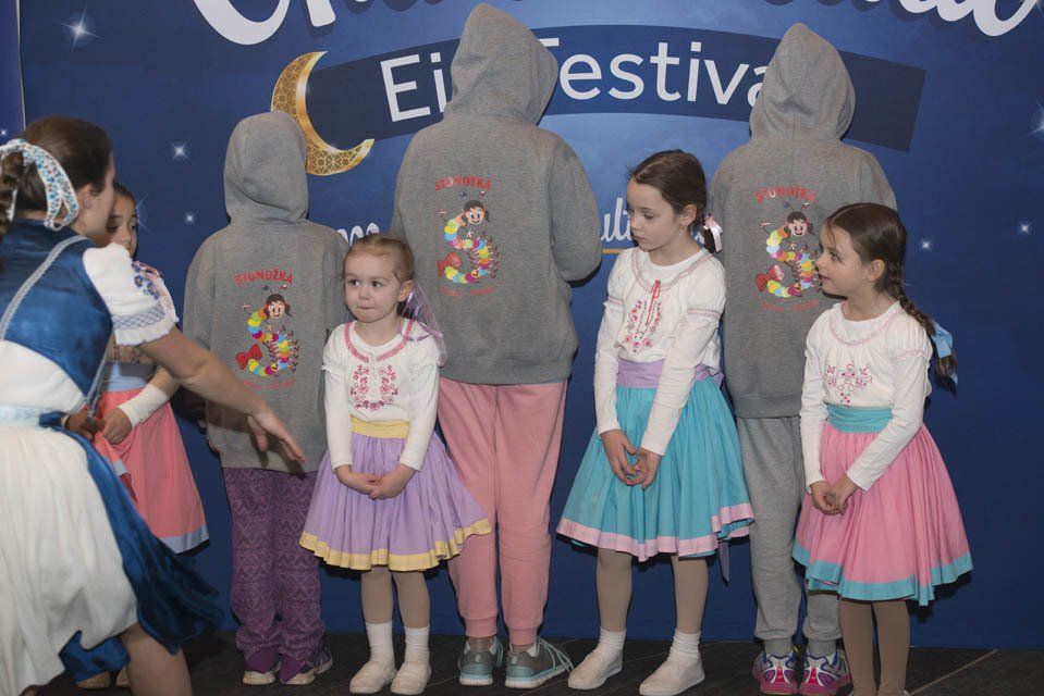 A group of children are standing in front of a sign that says festival
