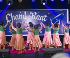 A group of women are dancing on a stage in front of a sign that says chand raat.