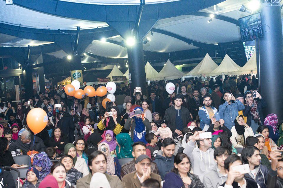A large group of people are sitting in a room with tents and balloons.