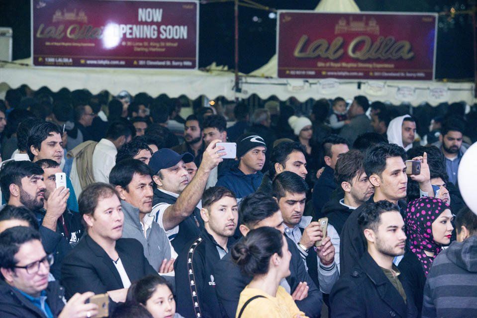 A crowd of people are gathered in front of a sign that says now opening soon