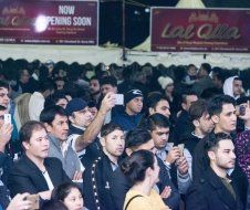 A crowd of people are standing in front of a sign that says now opening soon.