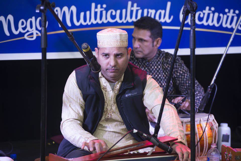 A man is playing a musical instrument in front of a sign that says multicultural activity