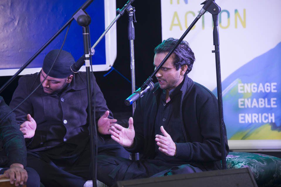 Two men are sitting in front of a sign that says engage enable enrich