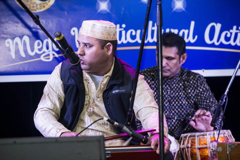 Two men are playing instruments in front of a sign that says mega