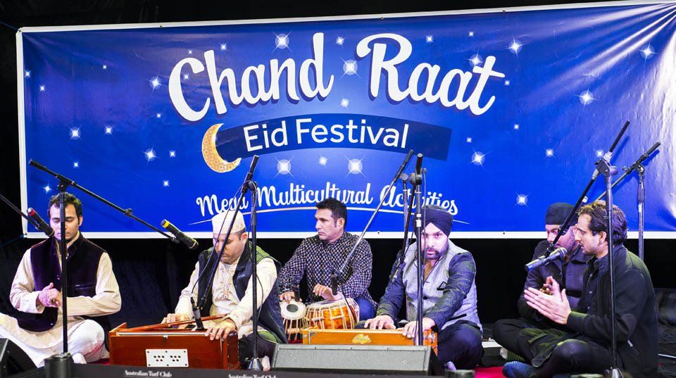 A group of men are playing instruments in front of a banner that says chand raat eid festival