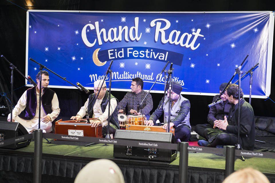 A group of men are playing instruments in front of a banner that says chand raat eid festival