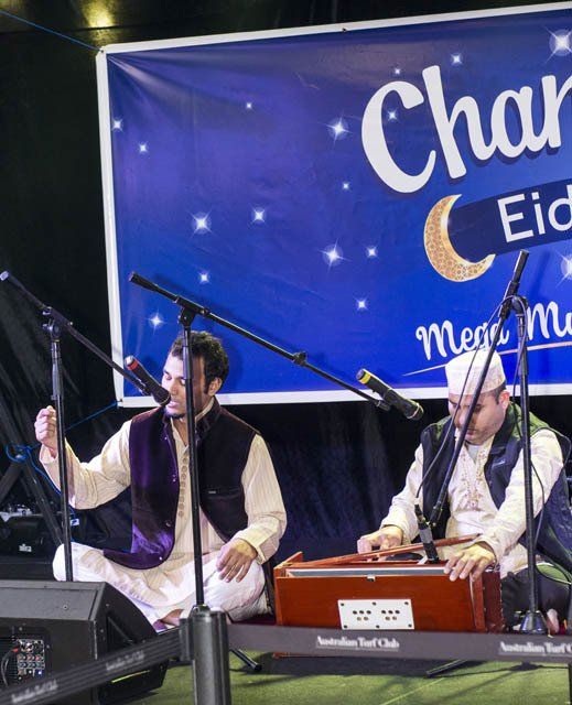 Two men are playing instruments in front of a banner that says char eid