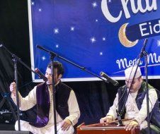 Two men are playing instruments in front of microphones on a stage.