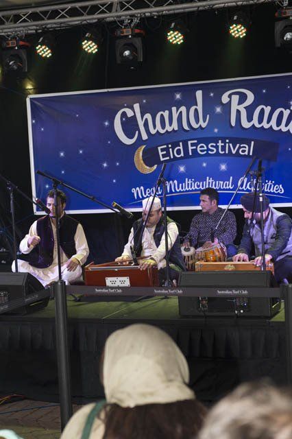 A group of men are playing instruments in front of a sign that says chand rad eid festival