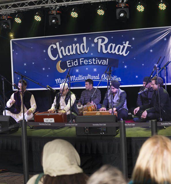A group of people playing instruments in front of a banner that says chand raat eid festival