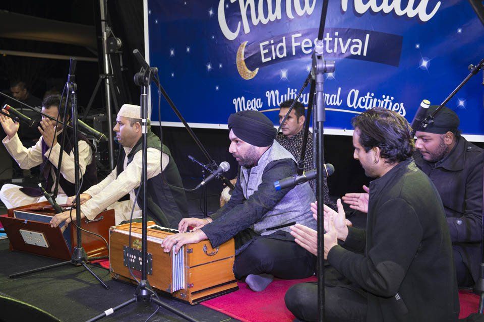 A group of men are playing instruments in front of a sign that says eid festival