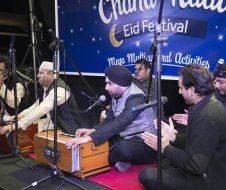 A group of men are playing instruments in front of a sign that says eid festival.