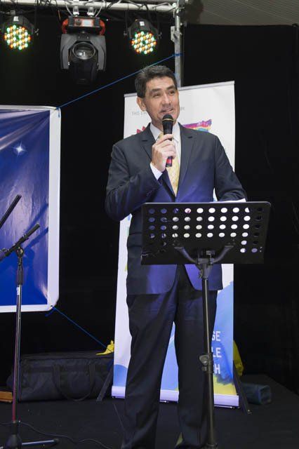 A man in a suit stands at a podium holding a microphone