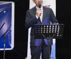 A man in a suit is standing at a podium holding a microphone.