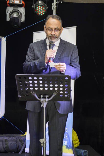 A man in a suit is standing at a podium holding a microphone.
