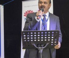A man in a suit and tie is standing at a podium holding a microphone.