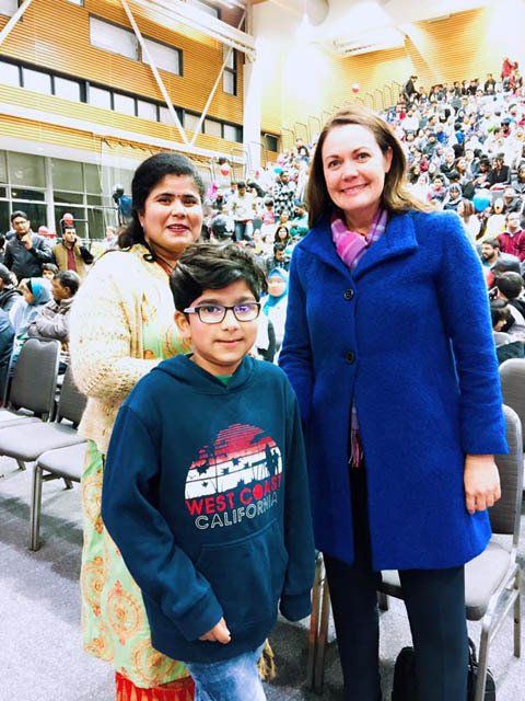 A woman in a blue coat stands next to a boy wearing a west coast california sweatshirt